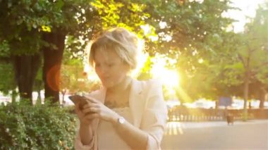 Çekici genç kadın parkta yürüyüş ve bir akıllı telefon kullanır