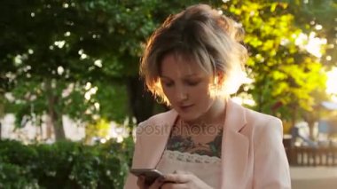 Çekici genç kadın parkta yürüyüş ve bir akıllı telefon kullanır