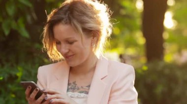 Güneşli gün parkta bir smartphone kullanarak çekici beyaz kadın sarışın