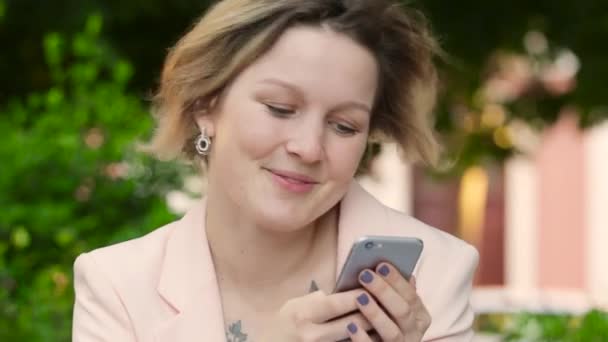Wanita kulit putih pirang yang menarik bekerja lepas dan menggunakan smartphone di taman pada hari yang cerah — Stok Video