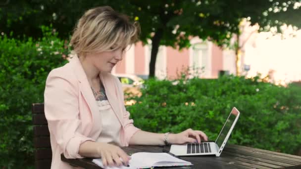 Atractiva rubia blanca que trabaja freelance con laptop y smartphone en el parque en un día soleado — Vídeo de stock