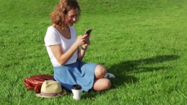 Çekici genç kadın'ın bahçesinde bir akıllı telefon güneşli gün kullanır.