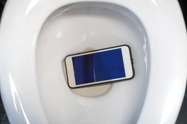 Sebuah smartphone putih jatuh ke dalam mangkuk toilet . Stok Gambar Bebas Royalti
