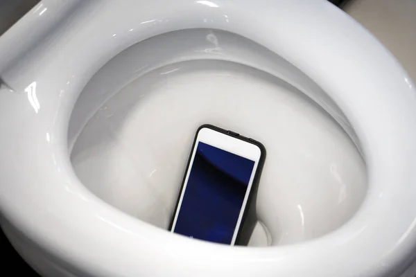 Um smartphone branco caiu em um vaso sanitário . Fotos De Bancos De Imagens Sem Royalties