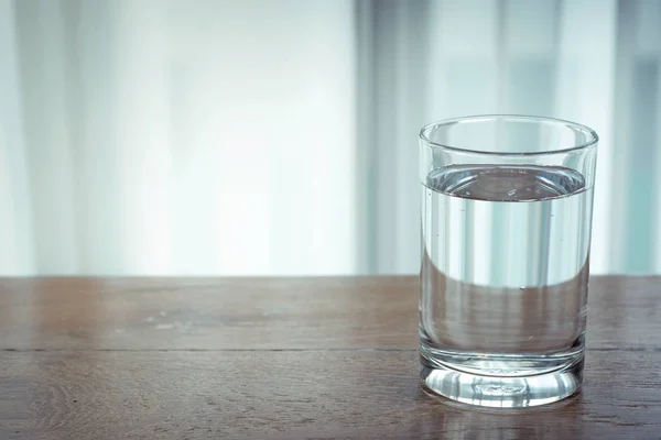 Glass of water on wooden table and light blurred background.
