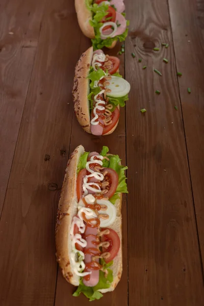 Sandwich aux saucisses et légumes sur une table en bois — Photo