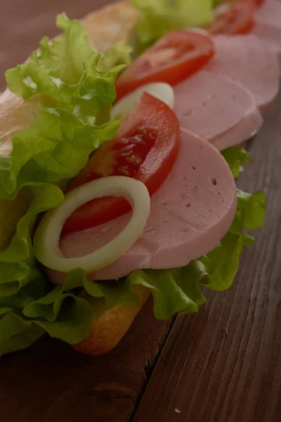 Сэндвич с колбасой и овощами на деревянном столе — стоковое фото