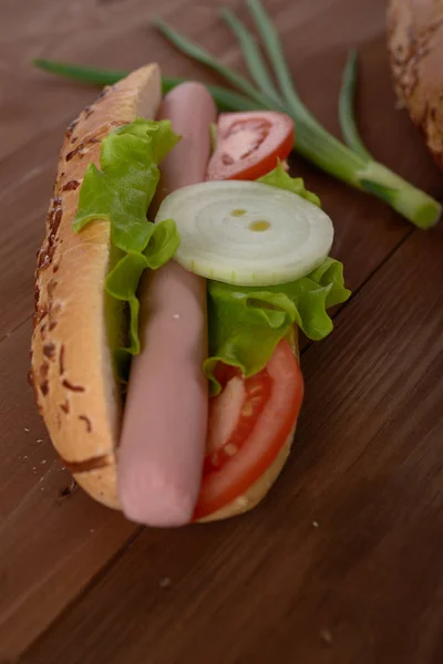 Panino con salsiccia e verdure su un tavolo di legno — Foto Stock