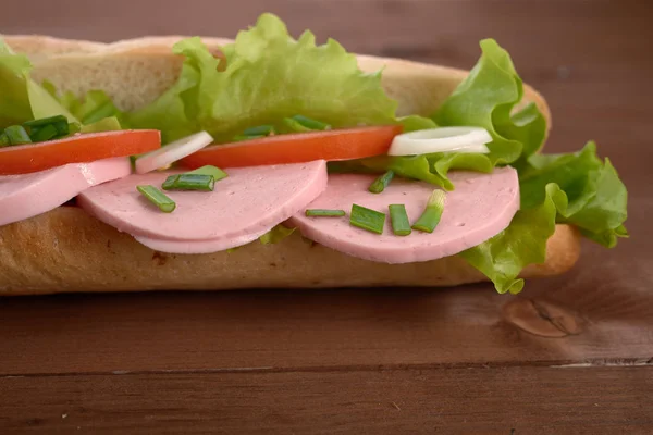 Sanduíche com linguiça e legumes em uma mesa de madeira — Fotografia de Stock