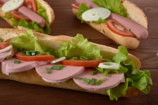 Sandwich aux saucisses et légumes sur une table en bois — Photo