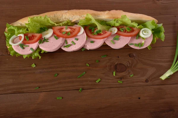 Сэндвич с колбасой и овощами на деревянном столе — стоковое фото