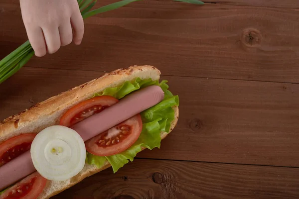 Panino con salsiccia e verdure su un tavolo di legno — Foto Stock