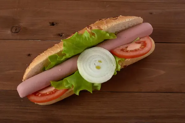 Panino con salsiccia e verdure su un tavolo di legno — Foto Stock