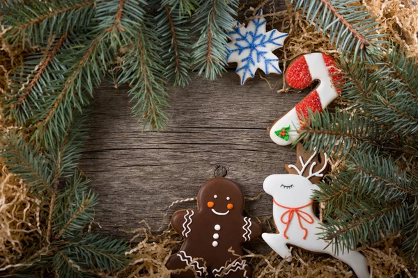 Christmas frame of pine branches. Decoration of painted ginger gingerbread. Gingerbread man, Christmas cane and snowman. Place under the text. Copy space.