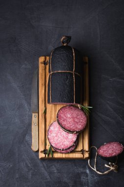 Tatlı sosis, dilimlenmiş otlar, kekik, biberiye ile kara kaplı tahta üzerinde. Vintage bıçak, tahta kesme vintage.