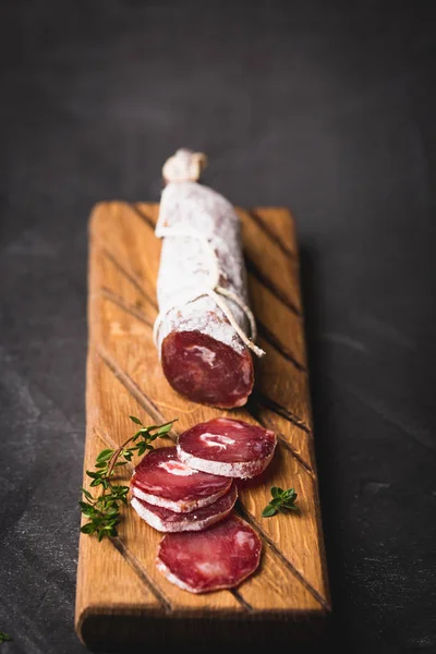 Fresh salami on a vintage Board. Vintage Cutlery fork and knife on a black coated background. Copy space.