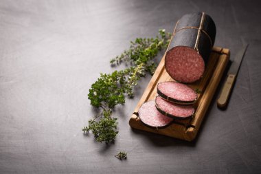 Tatlı sosis, dilimlenmiş otlar, kekik, biberiye ile kara kaplı tahta üzerinde. Vintage bıçak, tahta kesme vintage.