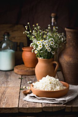 Ahşap arka plan üzerine bir tahta kaşık closeup ile bir kil tencerede peynir. Kil tencere taze süt ile. Uzay kopyalayın. Rustik tarzı.