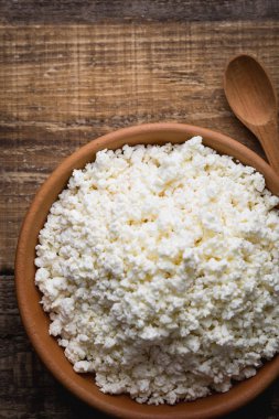 Ahşap arka plan üzerine bir tahta kaşık closeup ile bir kil tencerede peynir. Yukarıdan 90 derecelik bir açıyla vurdu. Kopya alanı.