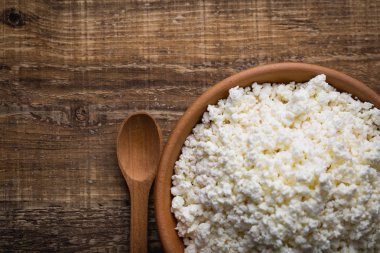 Ahşap arka plan üzerine bir tahta kaşık closeup ile bir kil tencerede peynir. Yukarıdan 90 derecelik bir açıyla vurdu. Kopya alanı.