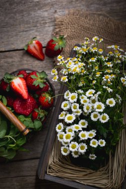 Çilek ahşap bir masa üzerinde. Papatya ve bir sepet ile bir yaz resmi.