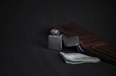 Composition of stylish men's things purse, lighter, one hundred dollar bills on a dark background clipart