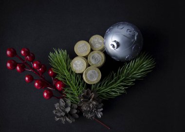 Siyah arka planda Noel oyuncakları ve bozuk paralar. Kazakistan tentesi ve Noel süsü. Sikkeler kazastan tenge 2020. Kazak parası ve yeni yıl oyuncakları, koniler, böğürtlenler.