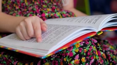 Renkli elbiseli küçük kız kitap okuyor. Çocuk okumayı öğreniyor..