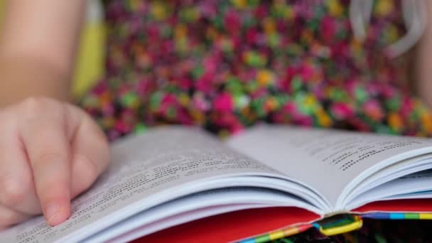 Una niña con un vestido colorido está leyendo un libro. Niño aprende a leer. — Vídeos de Stock