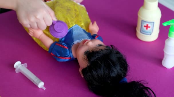 Mała dziewczynka bawiąca się w szpital. Dziecko lekarz traktuje lalkę na stole. Kwarantanna. — Wideo stockowe