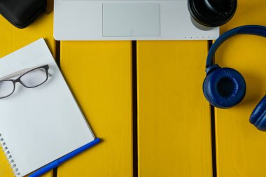 Sarı ahşap arka planda, kulaklık, kahve, not defteri ve dizüstü bilgisayarı olan düz bir kompozisyon. Giyin ya da podcast konsepti.