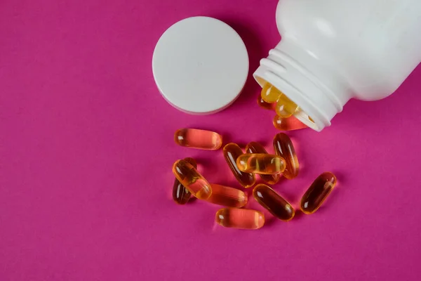 Sarı omega 3 balık yağı kapsülleri mor arka planda beyaz şişeden dökülüyor..