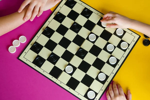 Çocuklar renkli bir masada dama oynarlar. Oğlan ve bir kız masa oyunlarında yarışıyorlar. Üst görünüm.