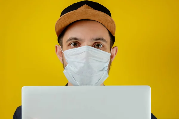 Tıbbi maskeli bir iş adamı dizüstü bilgisayarındaki haberlere bakıyor. Erkekler evde çalışır, kendilerini izole ederler, koronavirüsten karantinaya alınırlar..