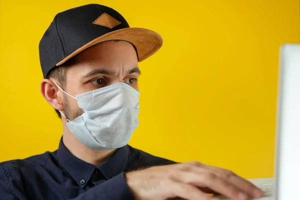 Tıbbi maskeli bir iş adamı dizüstü bilgisayarındaki haberlere bakıyor. Erkekler evde çalışır, kendilerini izole ederler, koronavirüsten karantinaya alınırlar..