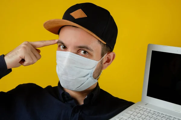 Man in a medical mask with a laptop, recommends online purchases, contactless delivery.