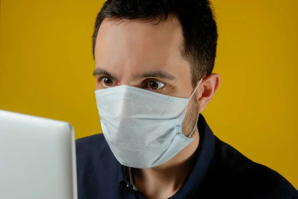 Tıbbi maskeli bir iş adamı laptopundaki haberlere şaşkınlıkla bakar. Erkekler evde çalışır, kendilerini izole ederler, koronavirüsten karantinaya alınırlar..