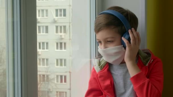 Ung Pojke Medicinsk Mask Tittar Genom Fönstret Och Lyssnar Musik — Stockvideo