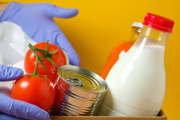 Gönüllü, sarı arka planda bir kutuda yiyecek seti gönderiyor. Karantina ve koronavirüs sırasında gıda bağışları. 