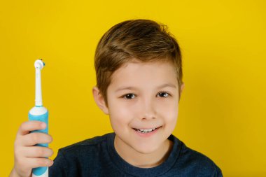 Elektrikli diş fırçasıyla dişlerini fırçalayan yakışıklı bir çocuk..