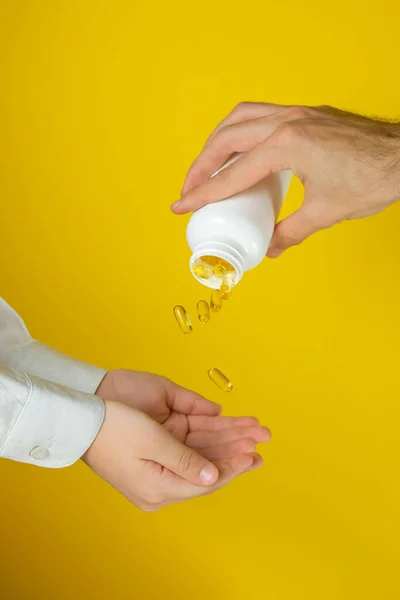 Sarı arka planda Omega 3 olan eller. Doktor çocuğa balık yağı verir..