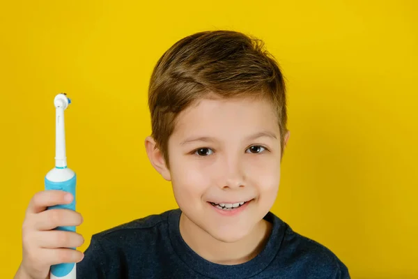 Elektrikli diş fırçasıyla dişlerini fırçalayan yakışıklı bir çocuk..