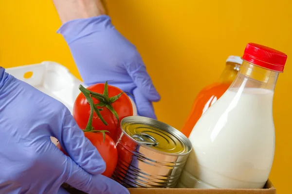 Gönüllü, ahşap bir arka planda bir kutuda yiyecek seti gönderir. Karantina ve koronavirüs sırasında gıda bağışları.