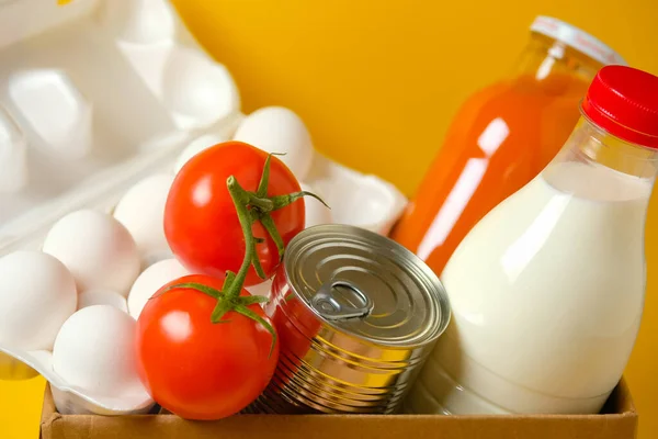 Sarı arka planda bir kutuda yiyecek seti. Karantina ve koronavirüs sırasında gıda bağışları.