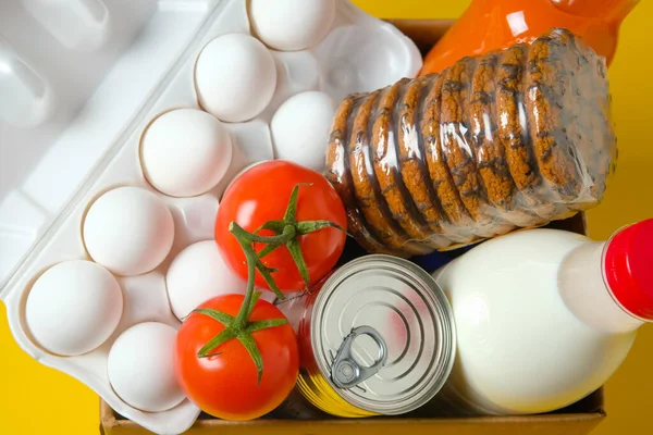 Sarı arka planda bir kutuda yiyecek seti. Karantina ve koronavirüs sırasında gıda bağışları.