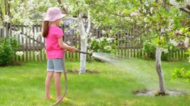 Şapkalı küçük kız, bir ağacı hortumla sulıyor.. 