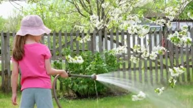 Şapkalı küçük kız, bir ağacı hortumla sulıyor.. 