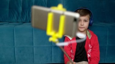 Yakışıklı çocuk telefonunda video bloğu hazırlıyor. Telefon, selfie çubuğu ve kulaklık kullanarak çocuk video görüşmeleri.