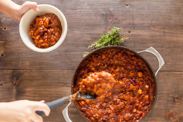 Hand Serving Scoop Of Chili From Iron Pot Into White Bowl