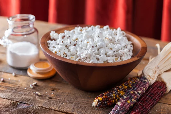 Frisch geknalltes Popcorn in Holzschale mit Körnern und Maiskolben auf dem Tisch — Stockfoto